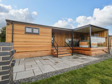 A wooden lodge with stairs leading to a covered deck area with glass railings at Enia Lodge 2 Llanelidan near Corwen