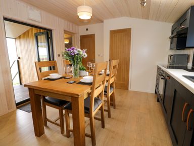 A kitchen dining area with a wooden table set for four with flowers and glassware at Enia Lodge 2 Llanelidan near Corwen