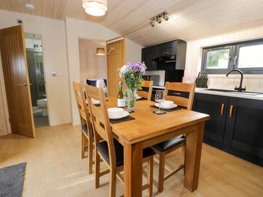 A kitchen and dining area with a wooden table set for four people and black cabinets at Enia (Lodge 2) in Llanelidan near Corwen