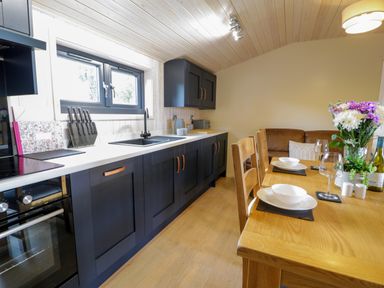 A kitchen with black cabinets white countertops and a dining table set with plates glasses and flowers at Enia Lodge 2 Llanelidan near Corwen