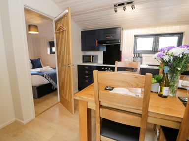 A dining table with chairs flowers and wine in a kitchen area next to a bedroom at Enia Lodge 2 in Llanelidan near Corwen