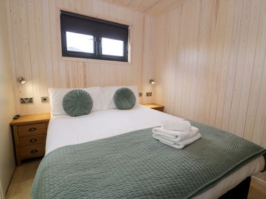 A bedroom with a double bed two round pillows bedside tables and folded towels on the bed at Enia Lodge 2 Llanelidan near Corwen