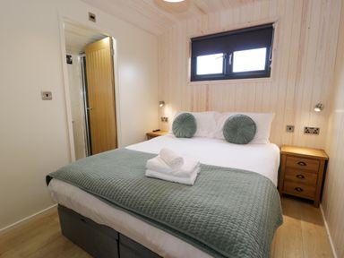 A bedroom with a bed with pillows and folded towels a wooden bedside table and a window at Enia Lodge 2 Llanelidan near Corwen