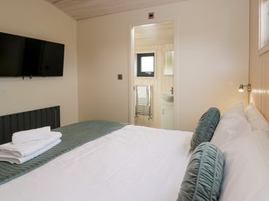 A bedroom with a bed with pillows and folded towels a wall mounted television and a doorway to a bathroom at Enia Lodge 2 Llanelidan near Corwen