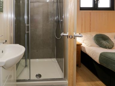 A bathroom with a shower enclosure and a sink next to a bedroom with a bed and wooden side table at Enia Lodge 2 Llanelidan near Corwen