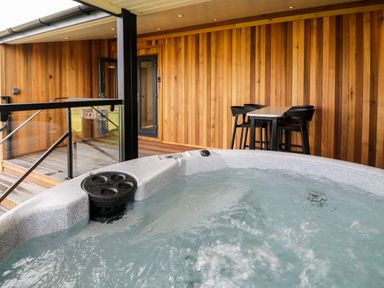 An outdoor wooden deck with a hot tub and a table with four chairs at Enia Lodge 2 in Llanelidan near Corwen
