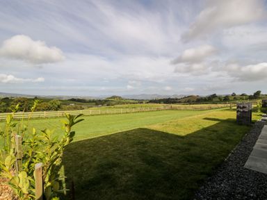 A grassy backyard with a wooden fence and hills in the distance at Enia Lodge 2 in Llanelidan near Corwen