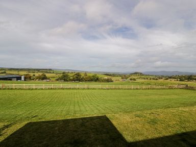A fenced grassy field with hills and trees in the background at Enia (Lodge 2) in Llanelidan near Corwen