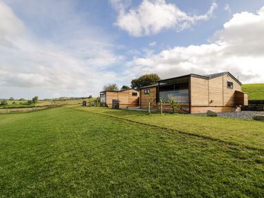 A grassy field with modern wooden lodges and a partly cloudy sky at Enia Lodge 2 in Llanelidan near Corwen