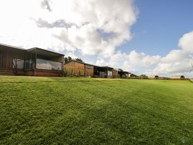 A row of wooden lodges on a grassy hill under a partly cloudy sky at Enia (Lodge 2) in Llanelidan near Corwen