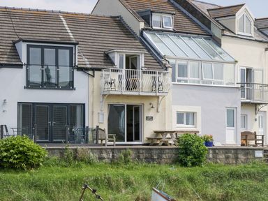 A row of houses with balconies and outdoor furniture by a grassy area at Lazey Cottage in Haverigg