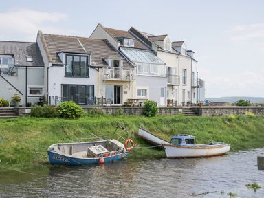 Boats moored in water near houses with balconies and outdoor seating at Lazey Cottage in Haverigg