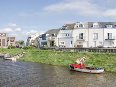 Boats tied to the shore in front of a row of houses by the water at Lazey Cottage in Haverigg