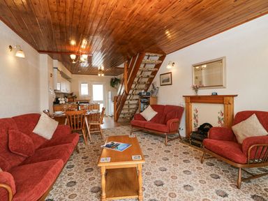 A living room with red sofas a wooden coffee table a dining table and chairs a staircase and a fireplace at Lazey Cottage in Haverigg