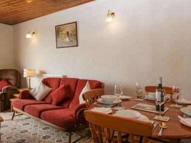 A living room with a red sofa and dining table set with plates and glasses at Lazey Cottage in Haverigg