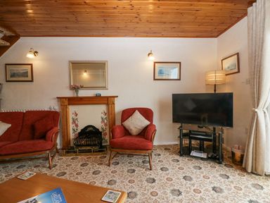 A living room with red chairs a fireplace a television and a wooden ceiling at Lazey Cottage in Haverigg