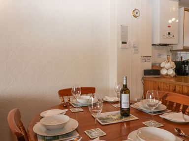 A dining table set with plates glasses cutlery and a bottle of wine in a kitchen at Lazey Cottage in Haverigg