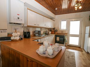 A kitchen with white cabinets wooden counters a coffee maker a kettle a stove and a door at Lazey Cottage in Haverigg