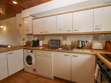 A kitchen with white cabinets appliances including a washing machine dishwasher kettle and toaster at Lazey Cottage in Haverigg