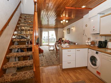 An open living space with a kitchen, dining table, carpeted stairs, and seating area at Lazey Cottage in Haverigg