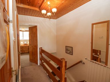 A hallway with wooden railing leading to a room with a wooden dresser and lamps at Lazey Cottage in Haverigg