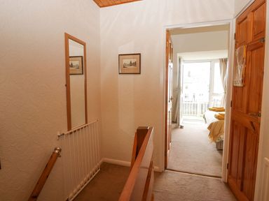 A hallway with a wooden railing and a small gate leading to a bedroom with a bed and open doors at Lazey Cottage in Haverigg