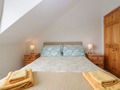 A bedroom with a double bed with floral bedding two bedside tables with lamps and wooden doors at Lazey Cottage in Haverigg