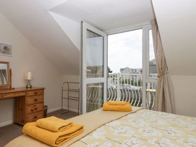 A bedroom with a bed holding folded towels a wooden dresser with a mirror and lamp and an open balcony door at Lazey Cottage in Haverigg