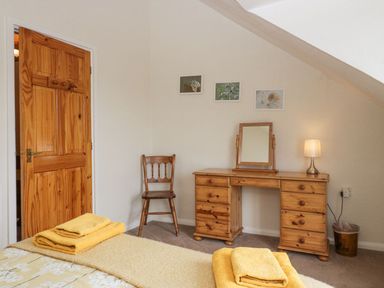 A bedroom with a wooden desk mirror chair and folded yellow towels on the bed at Lazey Cottage in Haverigg