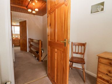 A hallway with wooden doors wooden chair wooden chest of drawers and a ceiling light at Lazey Cottage in Haverigg
