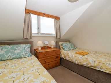 A bedroom with two single beds a wooden chest of drawers and a window at Lazey Cottage in Haverigg