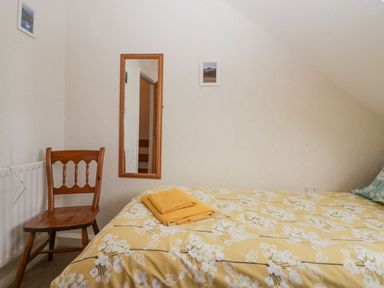 A bedroom with a wooden chair a wall mirror and a bed with yellow floral bedding and folded towels at Lazey Cottage in Haverigg