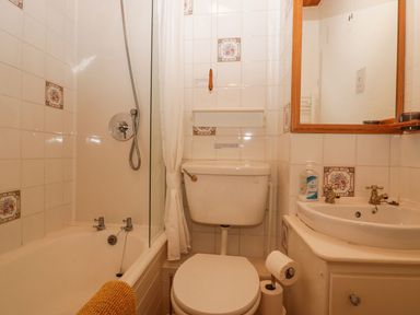A small bathroom with bathtub shower toilet sink and mirror at Lazey Cottage in Haverigg