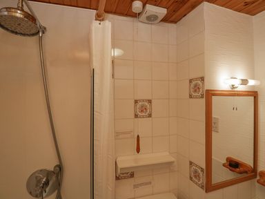 A bathroom with a shower area with curtain a tiled wall with decorative tiles a mirror with wooden frame and a wooden ceiling at Lazey Cottage in Haverigg