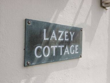 A metal sign reading Lazey Cottage mounted on a white wall at Lazey Cottage in Haverigg