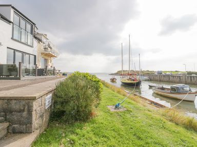 A waterfront with boats moored near a building and a grassy bank at Lazey Cottage in Haverigg