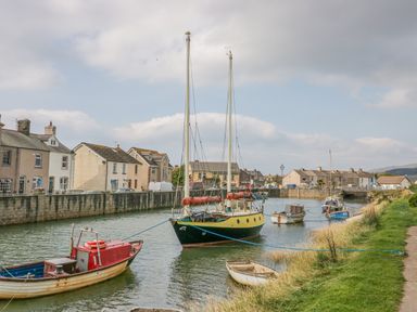A canal with several boats moored along the banks and houses lining the opposite side at Lazey Cottage in Haverigg