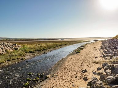 A sandy pathway beside a narrow river with rocks on one side and grass on the other at Lazey Cottage in Haverigg