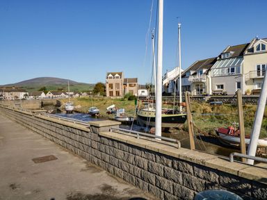 A canal with boats moored alongside houses and a stone wall walkway at Lazey Cottage in Haverigg