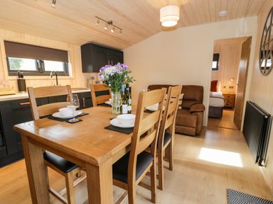 A dining area with wooden table and chairs set with plates glasses and flowers next to a kitchen with black cabinets at Math Lodge 3 Llanelidan near Corwen