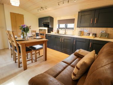 A kitchen and dining area with a wooden table set for four and dark cabinets at Math Lodge 3 in Llanelidan near Corwen