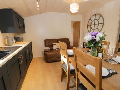 A kitchen and dining area with wooden dining table and chairs flowers on table and brown sofa at Math Lodge 3 Llanelidan near Corwen
