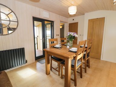 A dining area with a wooden table and four chairs set with plates glasses and flowers at Math Lodge 3 Llanelidan near Corwen