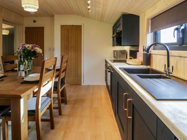 A kitchen and dining area with wooden table and chairs black cabinets and a sink at Math Lodge 3 Llanelidan near Corwen