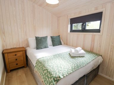 A bedroom with a double bed side table window and wooden panel walls at Math Lodge 3 Llanelidan near Corwen