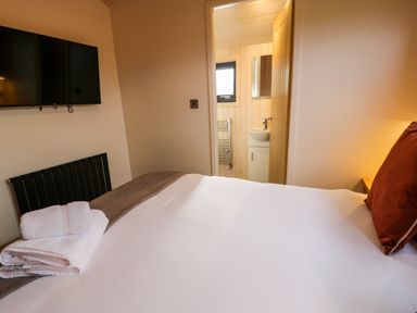 A bedroom with a bed folded towels a wall-mounted television and an open door leading to a bathroom at Math Lodge 3 Llanelidan near Corwen