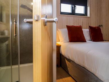 A bedroom with a bed and red pillows next to a bathroom with a glass shower door at Math Lodge 3 Llanelidan near Corwen