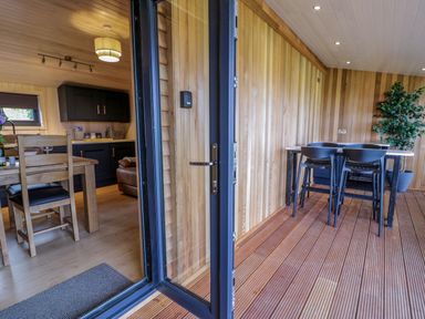 A kitchen and dining area with wooden dining table and chairs and an adjacent room with a table and chairs on a wooden floor at Math Lodge 3 in Llanelidan near Corwen