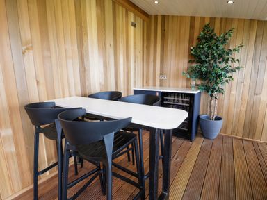 A dining area with a white table and four black chairs next to a cabinet and a potted plant at Math Lodge 3 in Llanelidan near Corwen