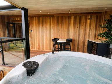 A covered outdoor area with a hot tub a small table with four black chairs wooden walls and a cabinet with a plant at Math Lodge 3 Llanelidan near Corwen